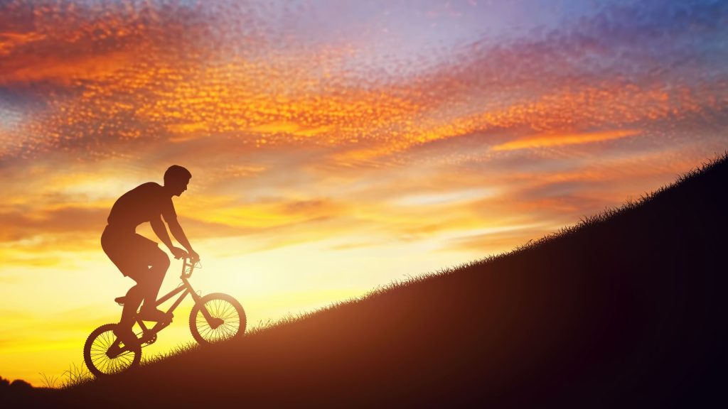 Man riding a BMX bike uphill against the sunset