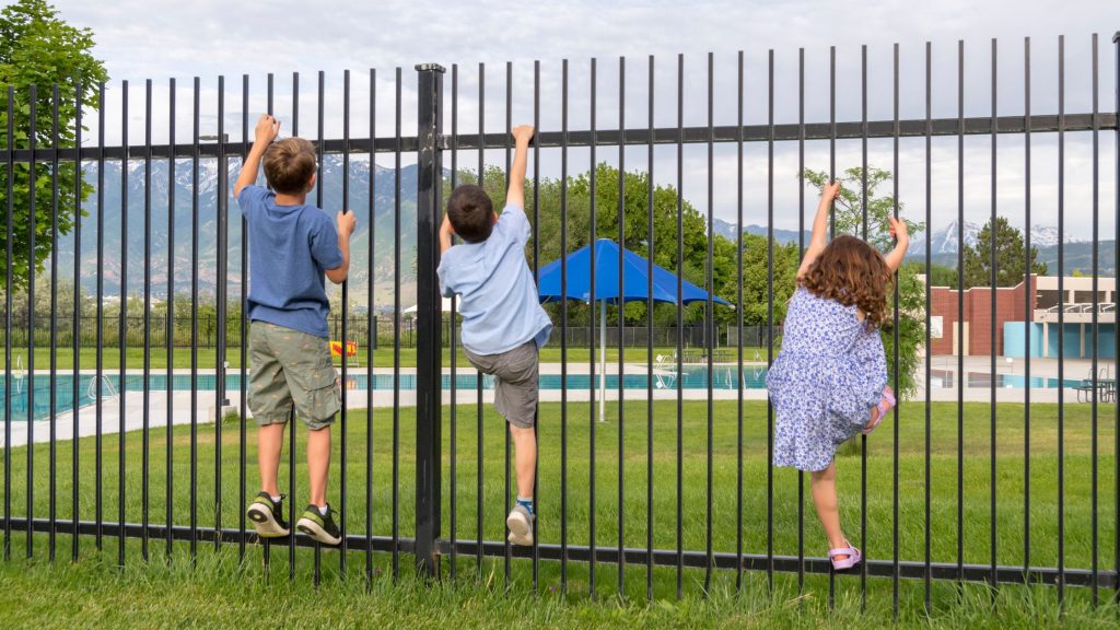 Kids trying to climb a pool fence but it is too high
