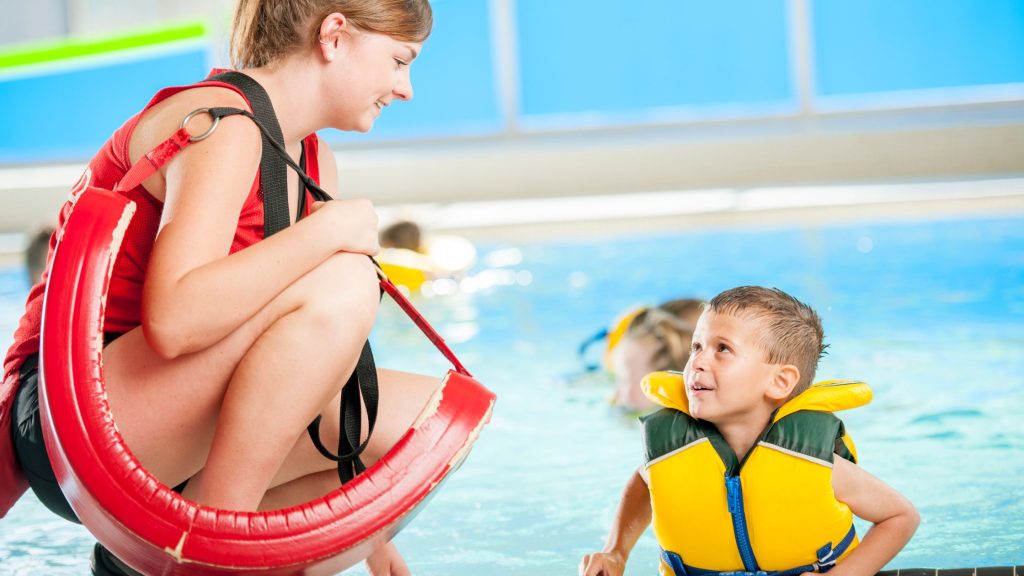 Lifeguard with young boy in a yellow life jacket at the pool