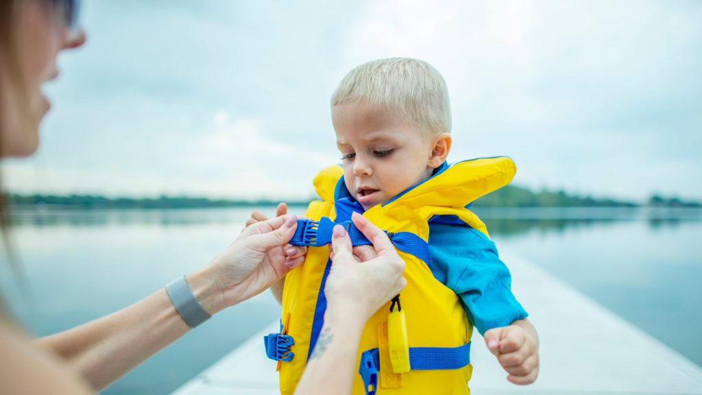 Young boy getting lifejacket secured by mom