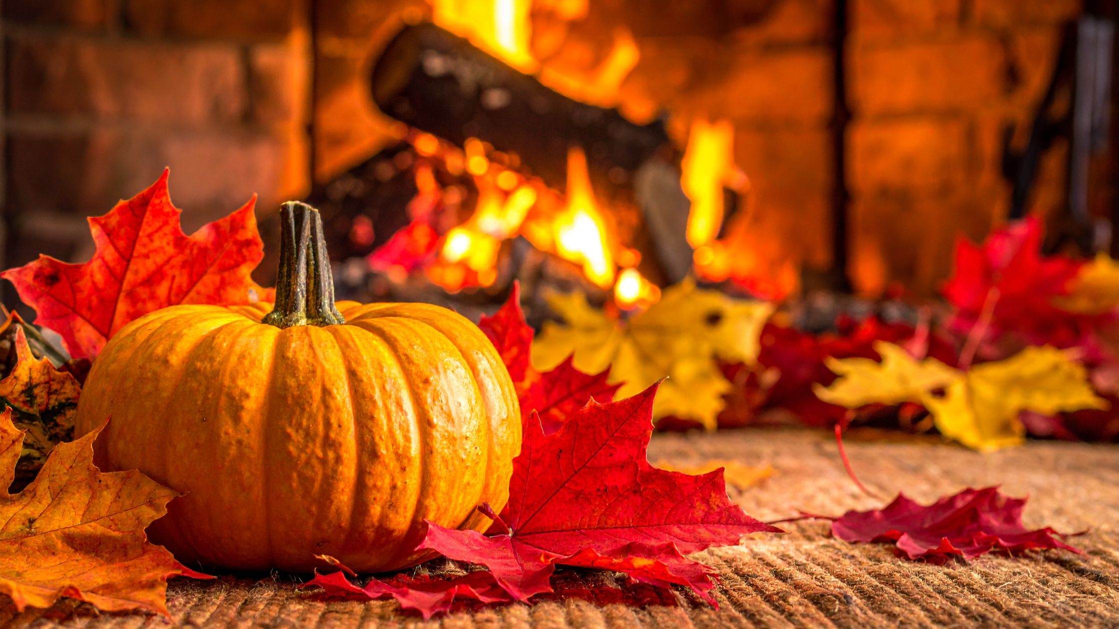 Pumpkin by the fireplace surrounded by autumn leaves